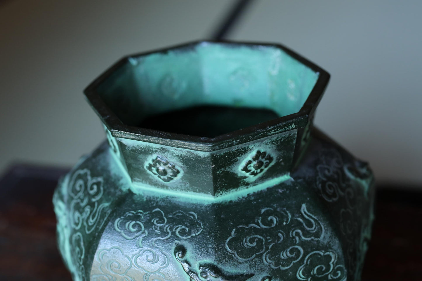 A close-up view of a green, octagonal vase with intricate designs and patterns.