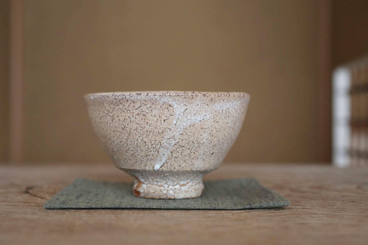 A white ceramic bowl with a textured surface sits on a green cloth on a wooden table.