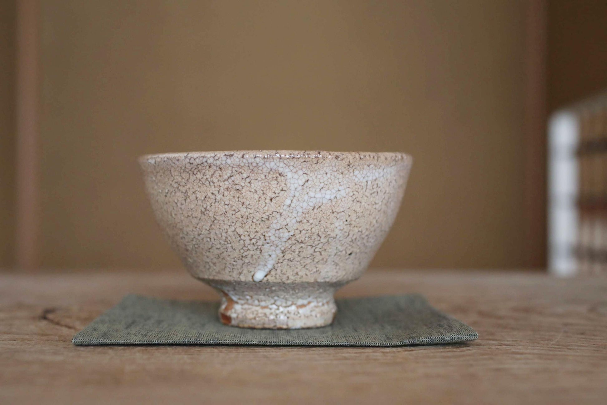 A white ceramic bowl with a textured surface sits on a green cloth on a wooden table.