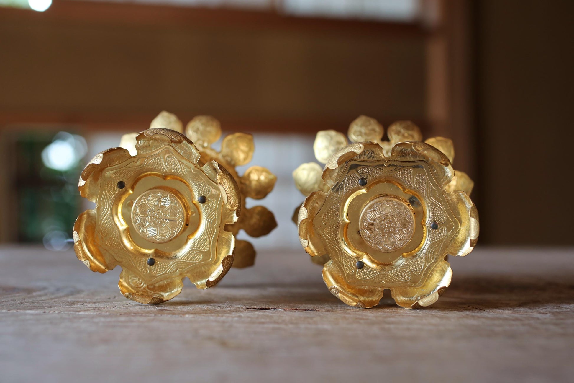 two ornate golden flower-shaped objects placed on a wooden surface.