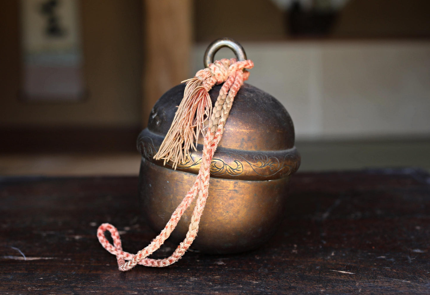 An old, round metal bell with a decorative design on its surface, resting on a wooden surface.