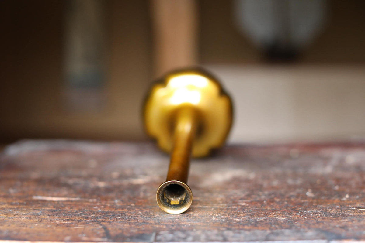 A close-up view of a golden-colored metal object, possibly a pipe or tube, resting on a wooden surface.