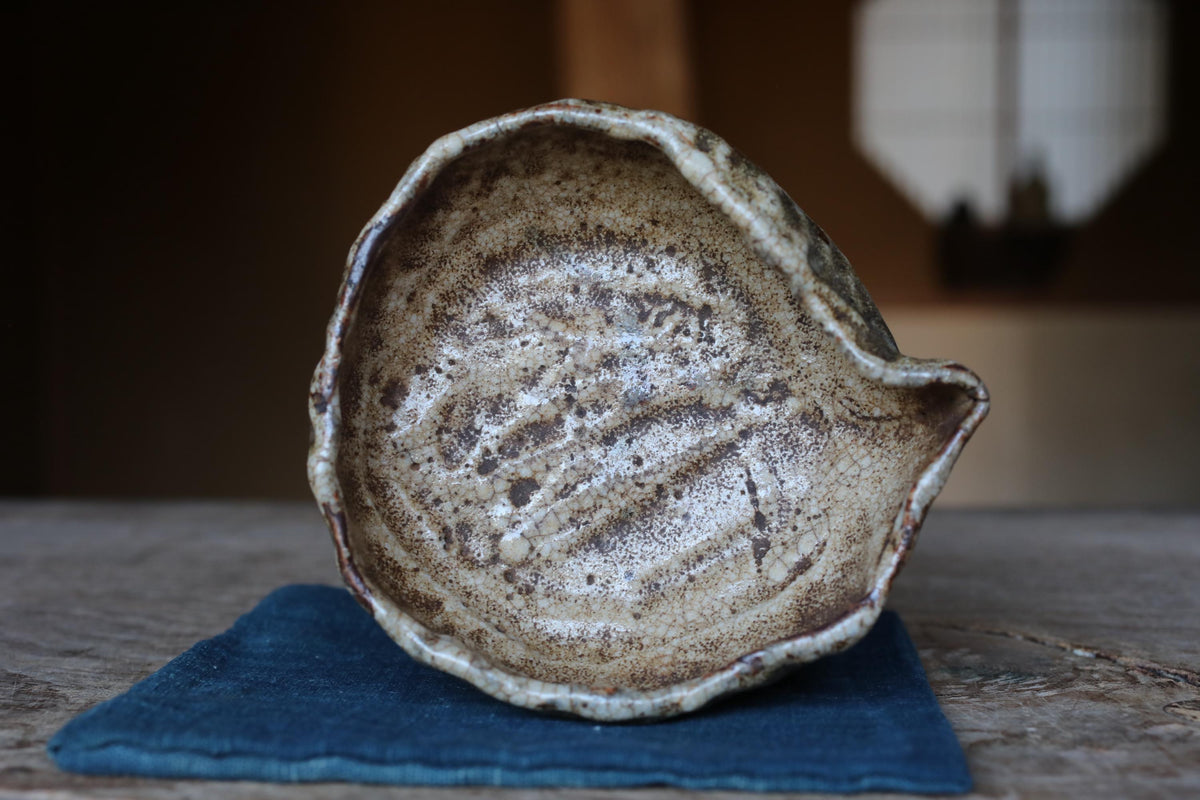 A ceramic bowl with a textured surface sits on a blue cloth on a wooden surface.