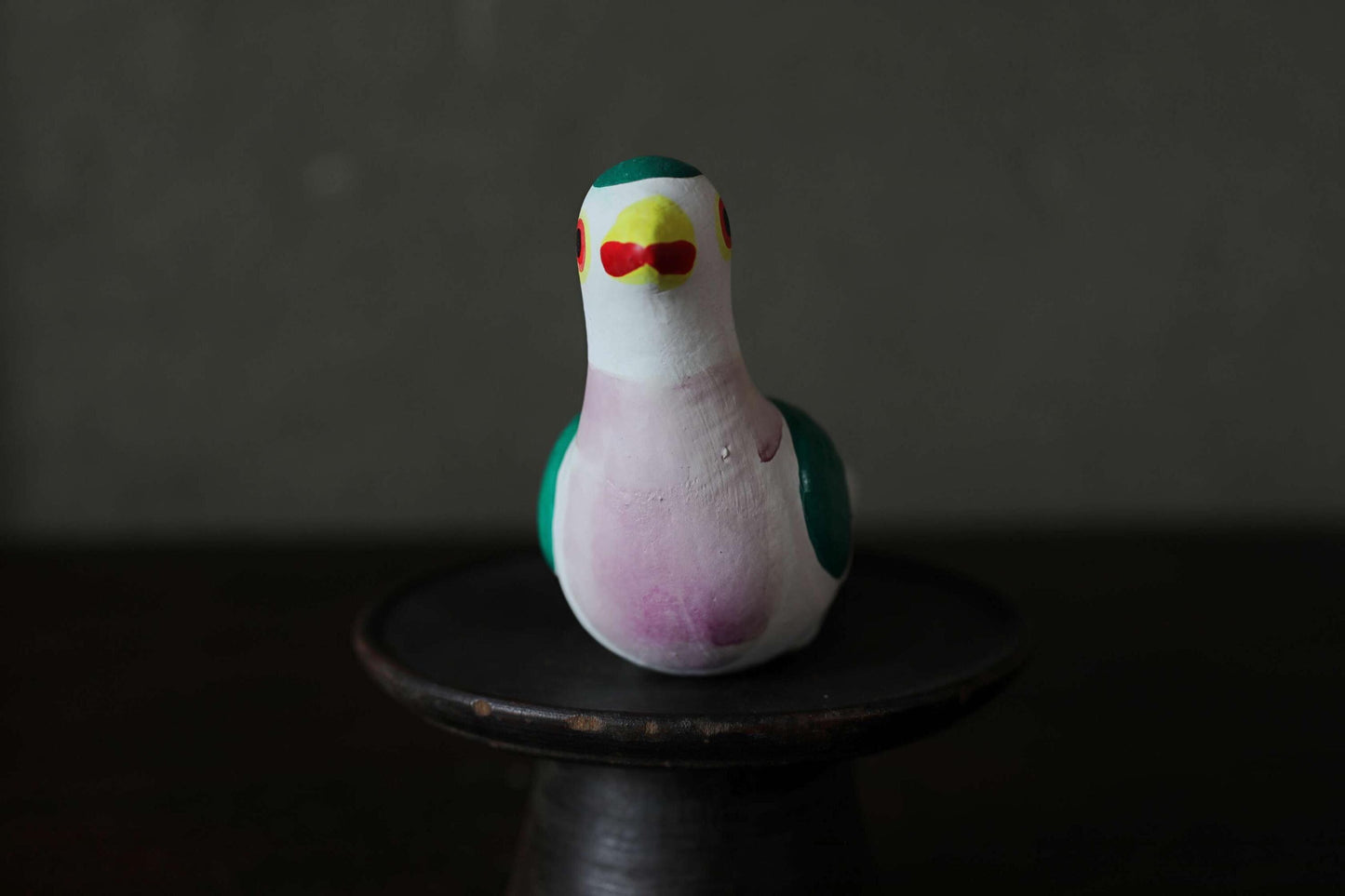 A colorful ceramic bird figurine is sitting on a dark surface.