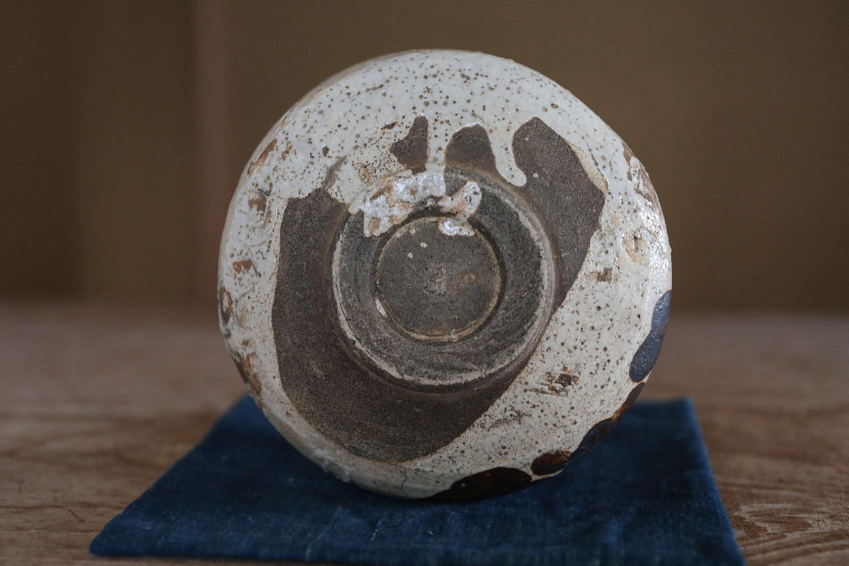 A white and brown ceramic bowl with a distinctive design sits on a blue cloth on a wooden surface.
