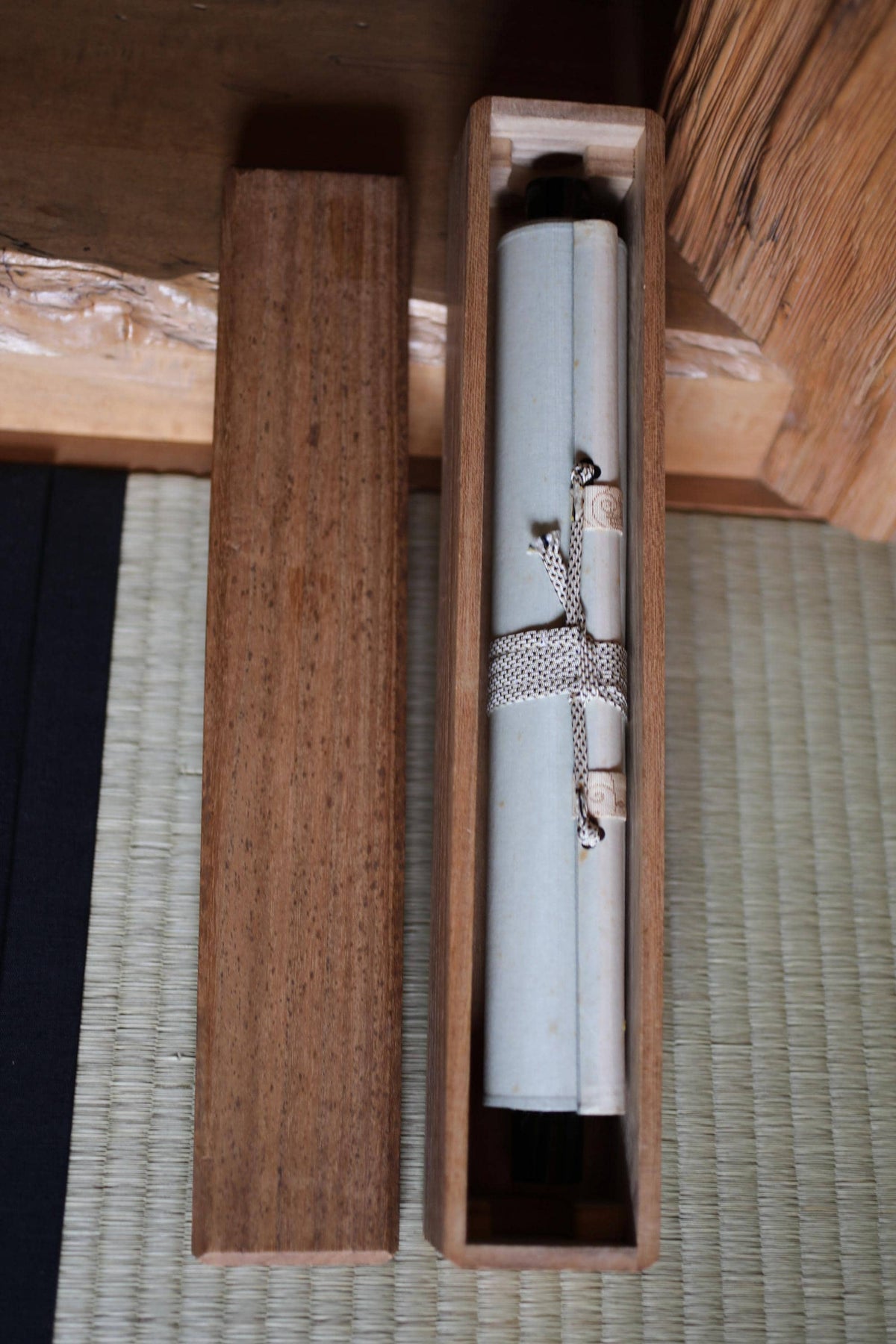 a wooden box with a rolled-up scroll or document inside, placed on a woven mat or mat-like surface.