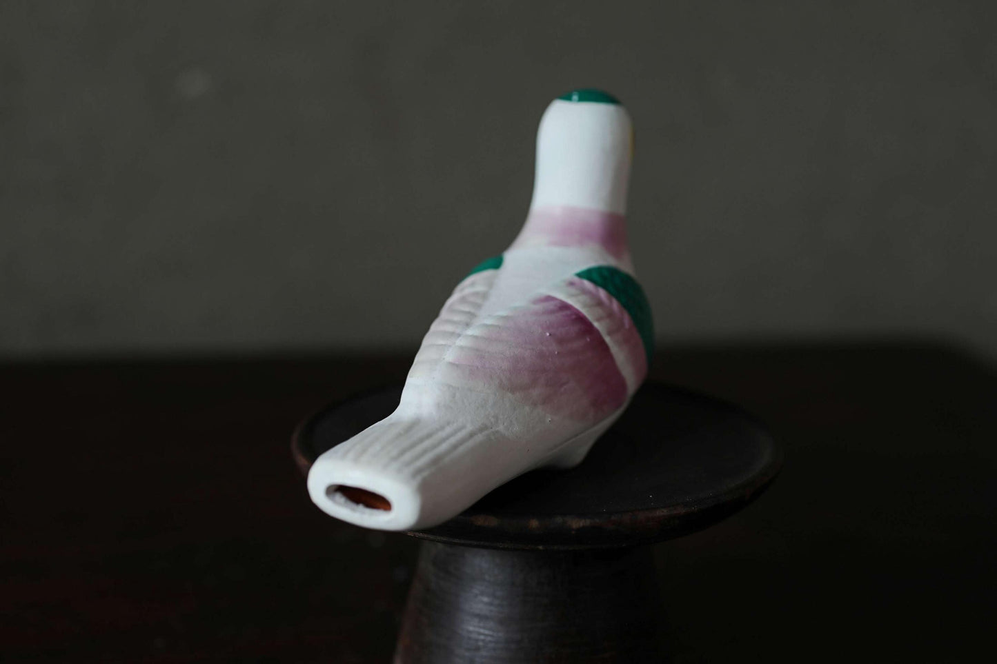 A ceramic bird figurine with a white body and green accents is sitting on a dark surface.