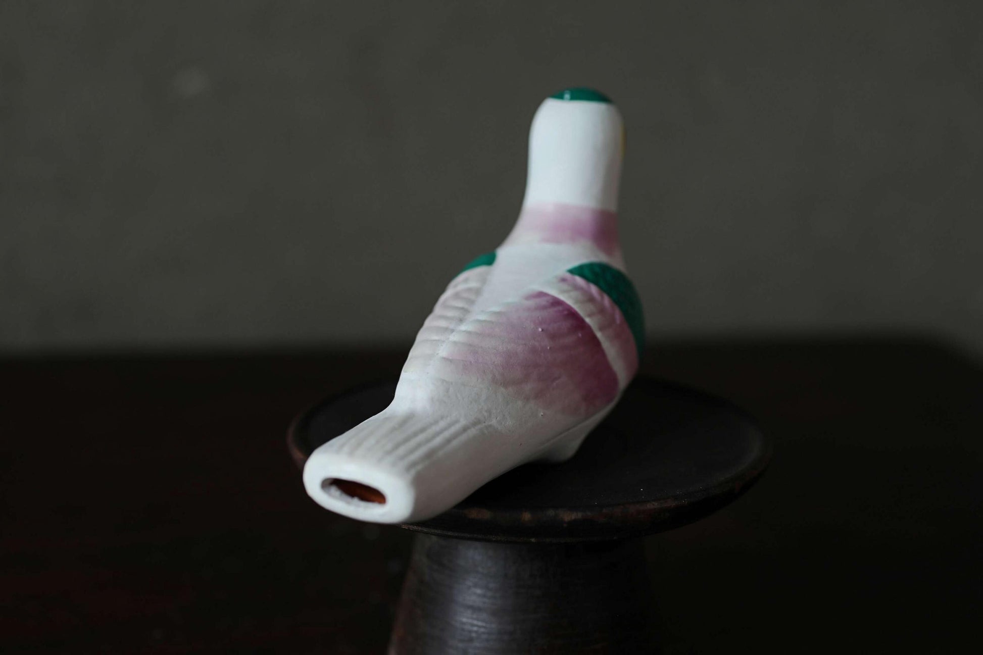 A ceramic bird figurine with a white body and green accents is sitting on a dark surface.