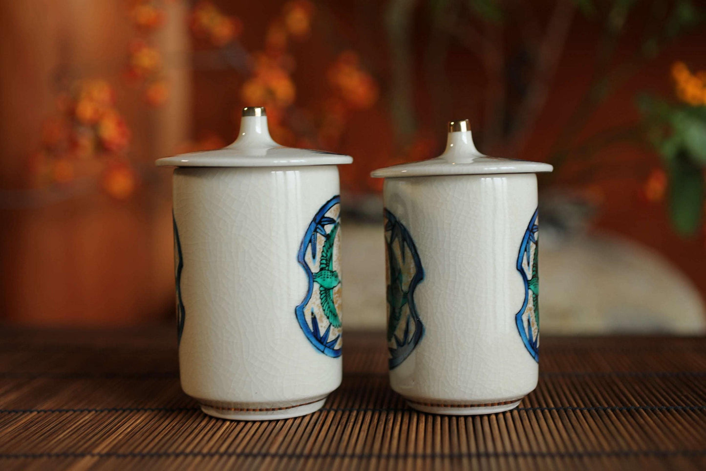 Two white ceramic containers with blue and green designs on them, placed on a wooden surface.