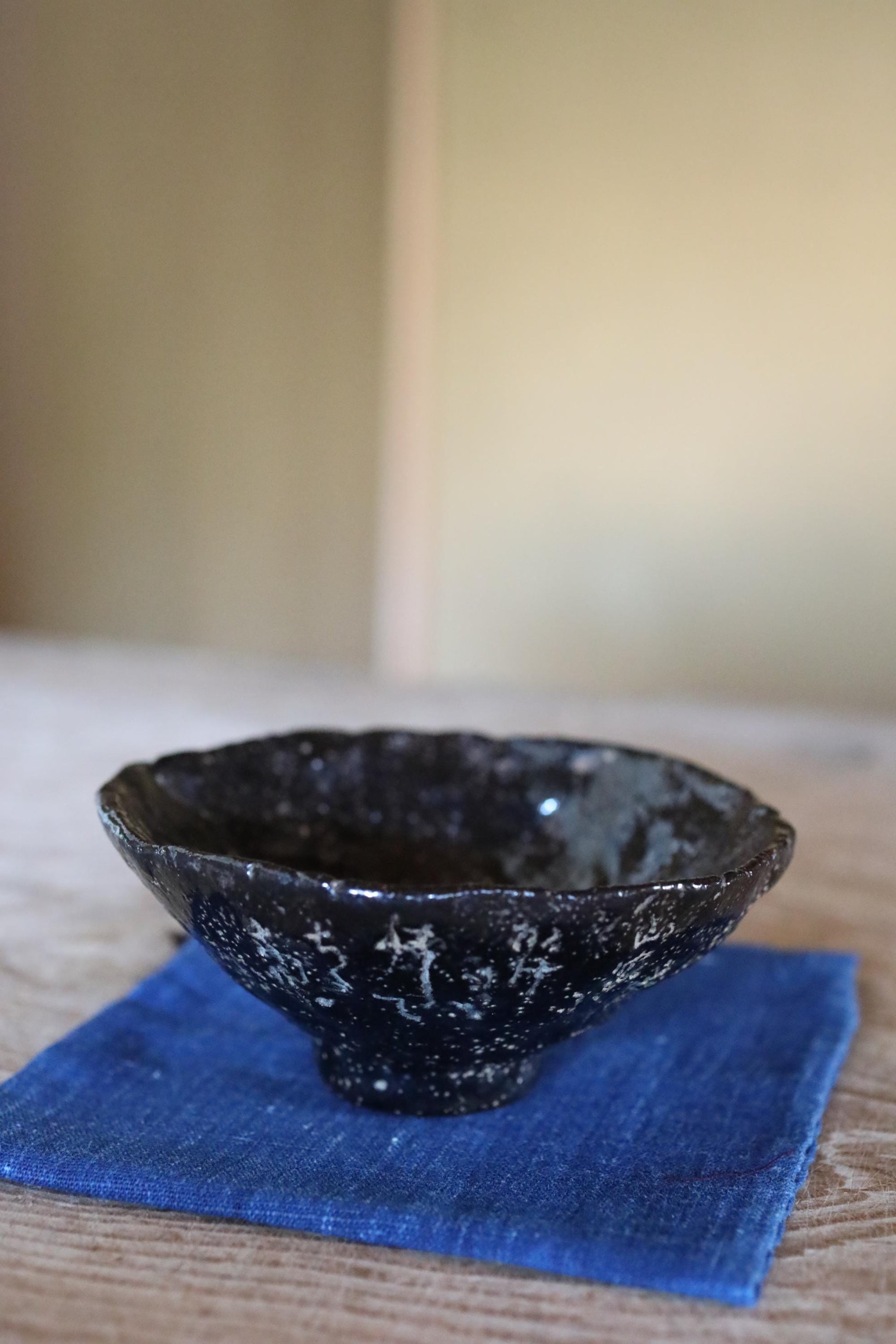 A black ceramic bowl with a textured surface sits on a blue cloth on a wooden table.