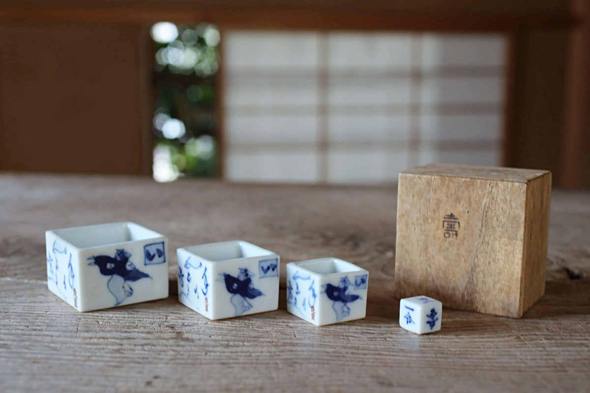 a collection of ceramic objects, including three small square containers and a wooden box, arranged on a wooden surface.