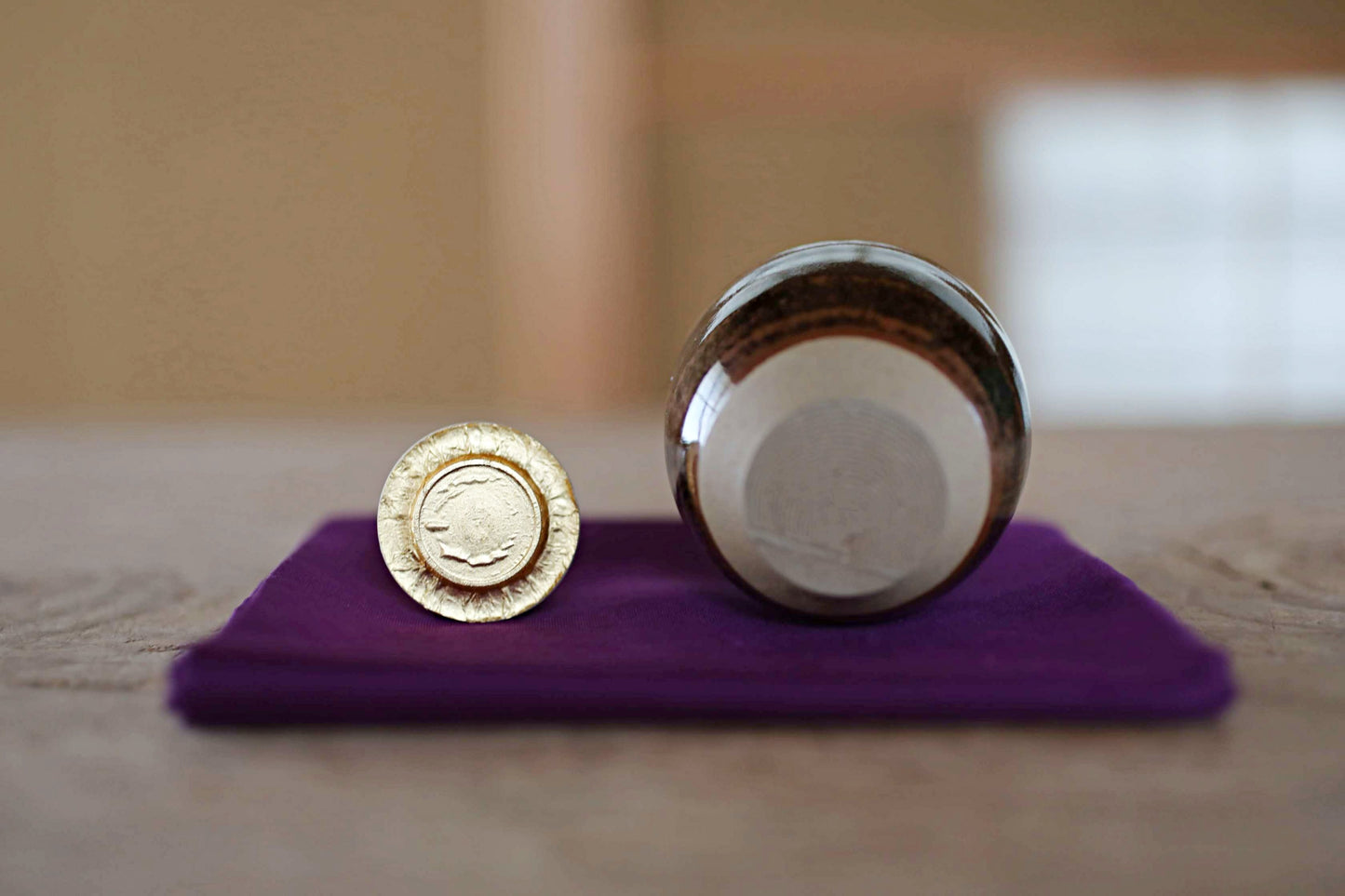 a small gold-colored coin and a small glass jar or bottle placed on a purple cloth on a wooden surface.