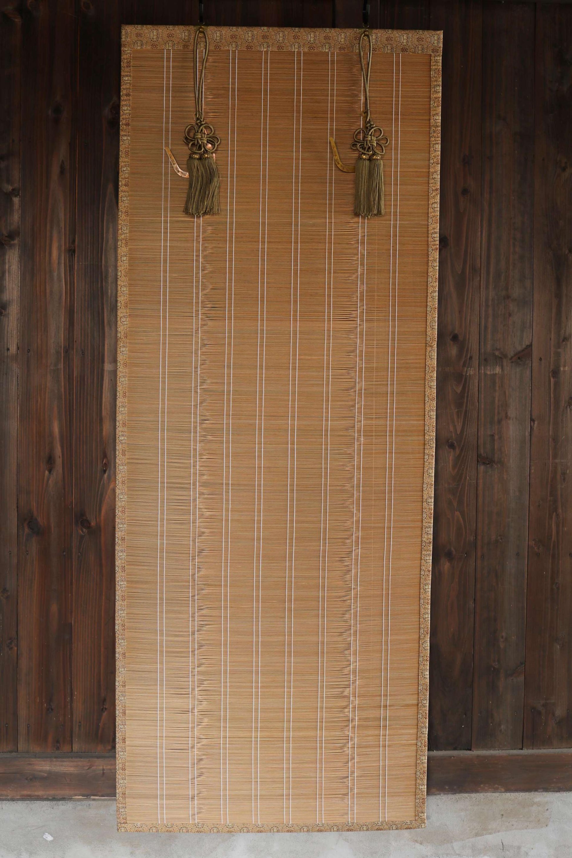 a bamboo blind with tassels hanging from the top, set against a wooden wall.