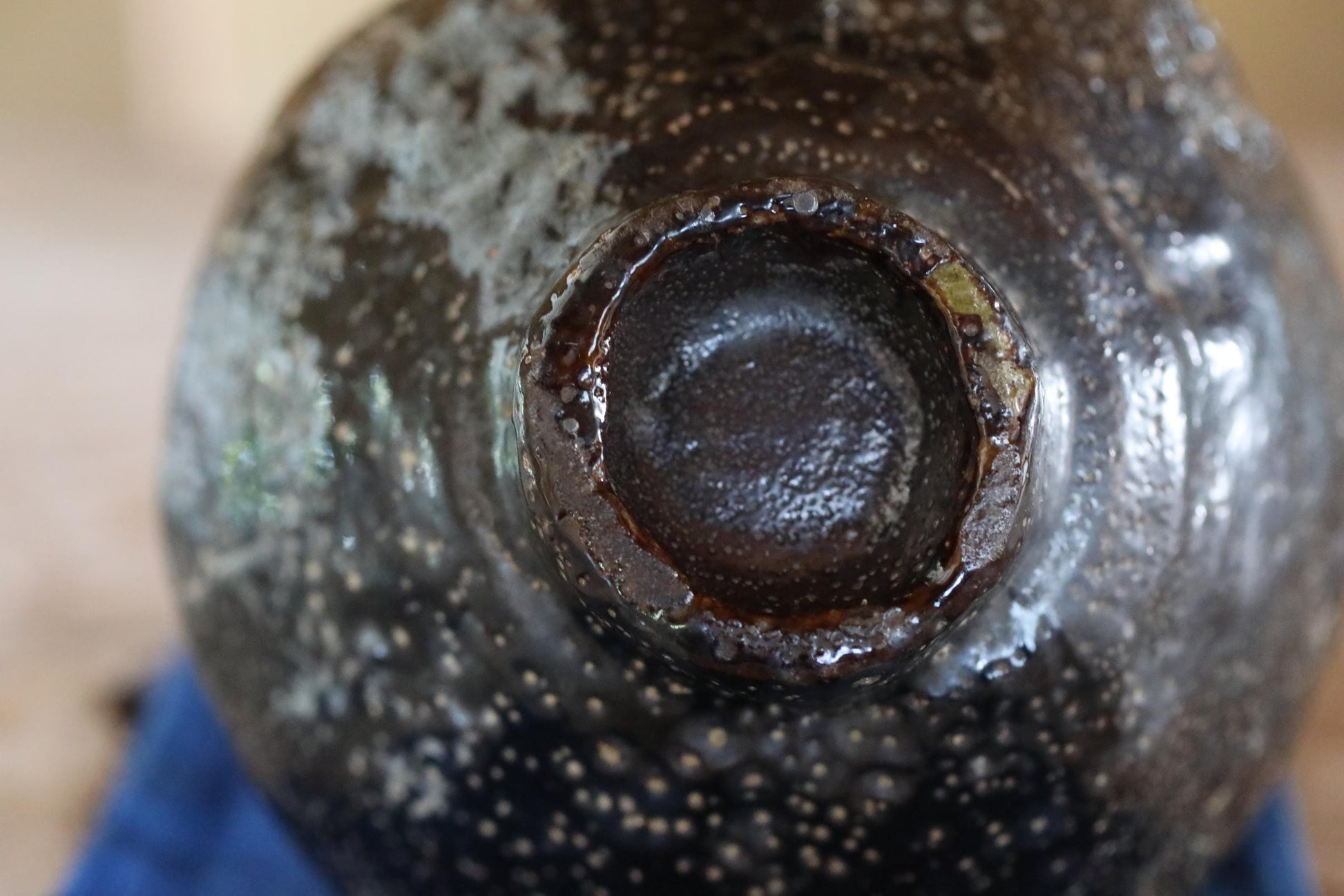 A close-up view of a dark, speckled ceramic object, possibly a vase or bowl, with a hole in the center.