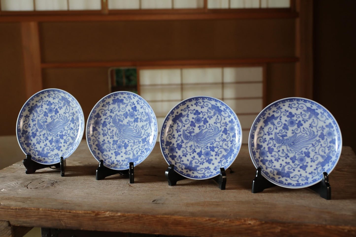 A row of four blue and white patterned plates with a bird design, displayed on a wooden surface.