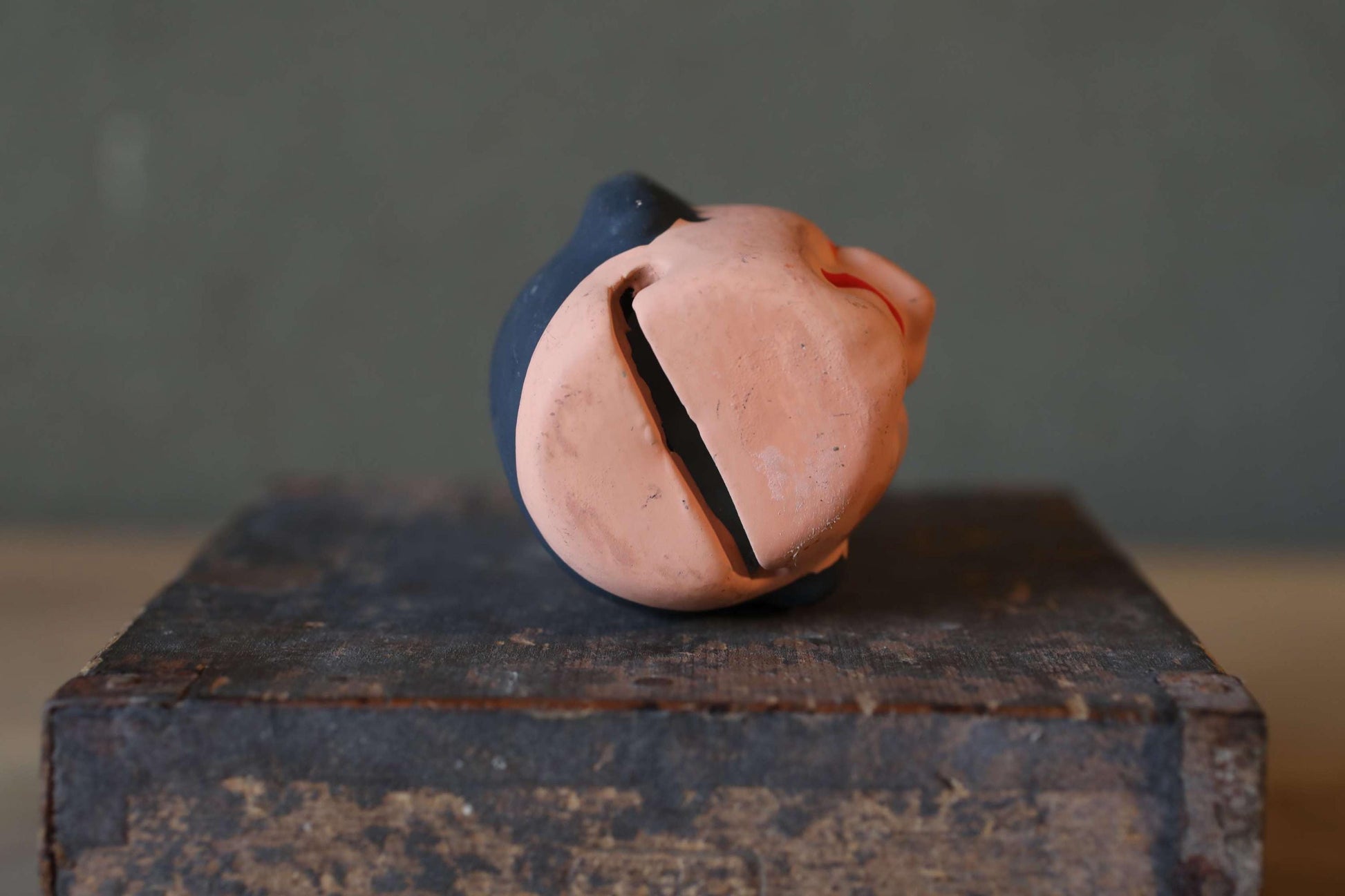 A broken toy or figurine with a cracked face and a blue body, sitting on a wooden surface.