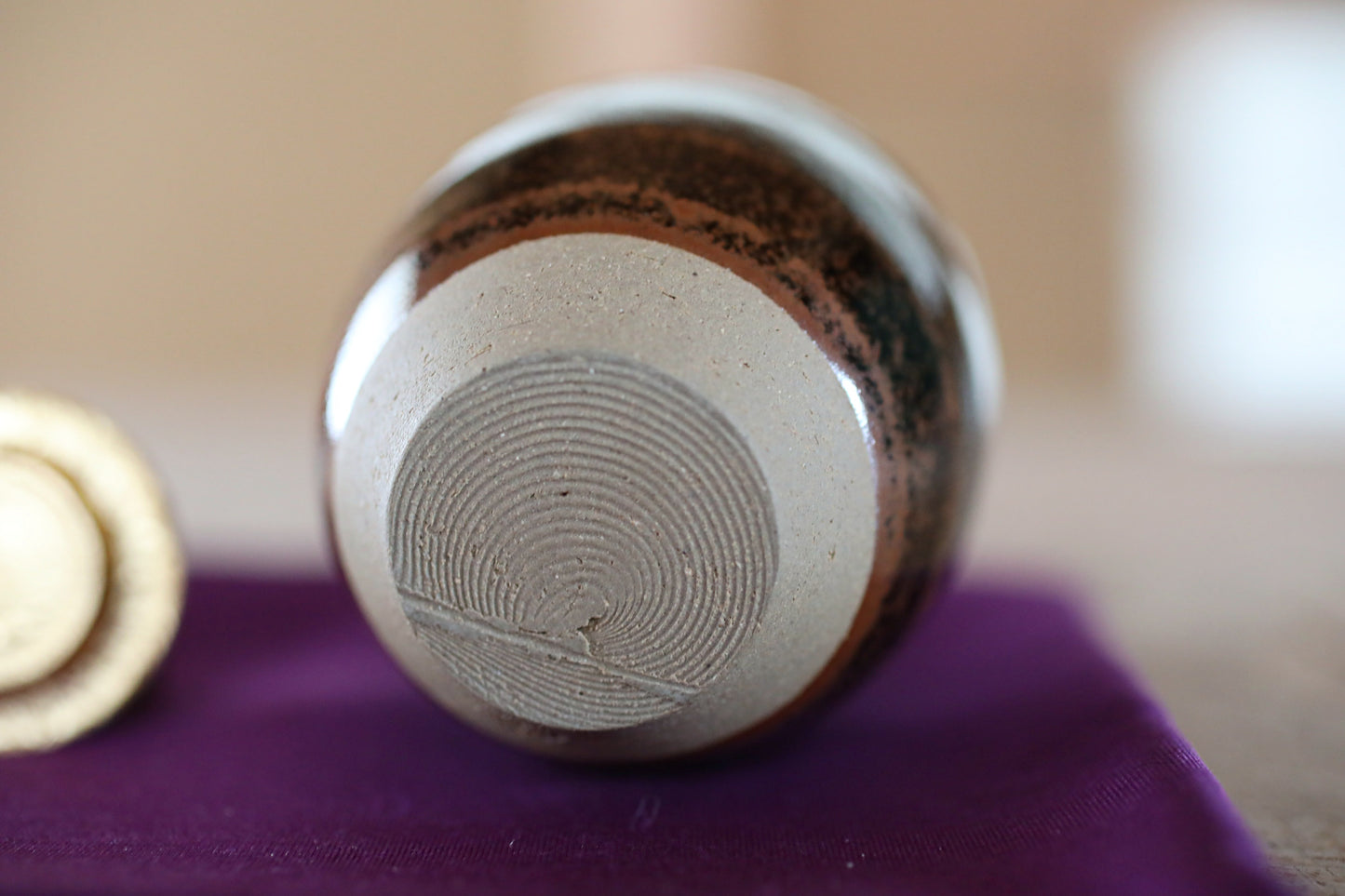 A close-up image of a ceramic object with a textured surface, resting on a purple cloth.