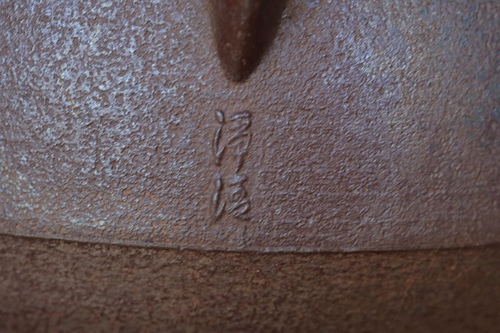 a close-up view of a textured surface, possibly a piece of pottery or metal, with a carved symbol or text etched into it.