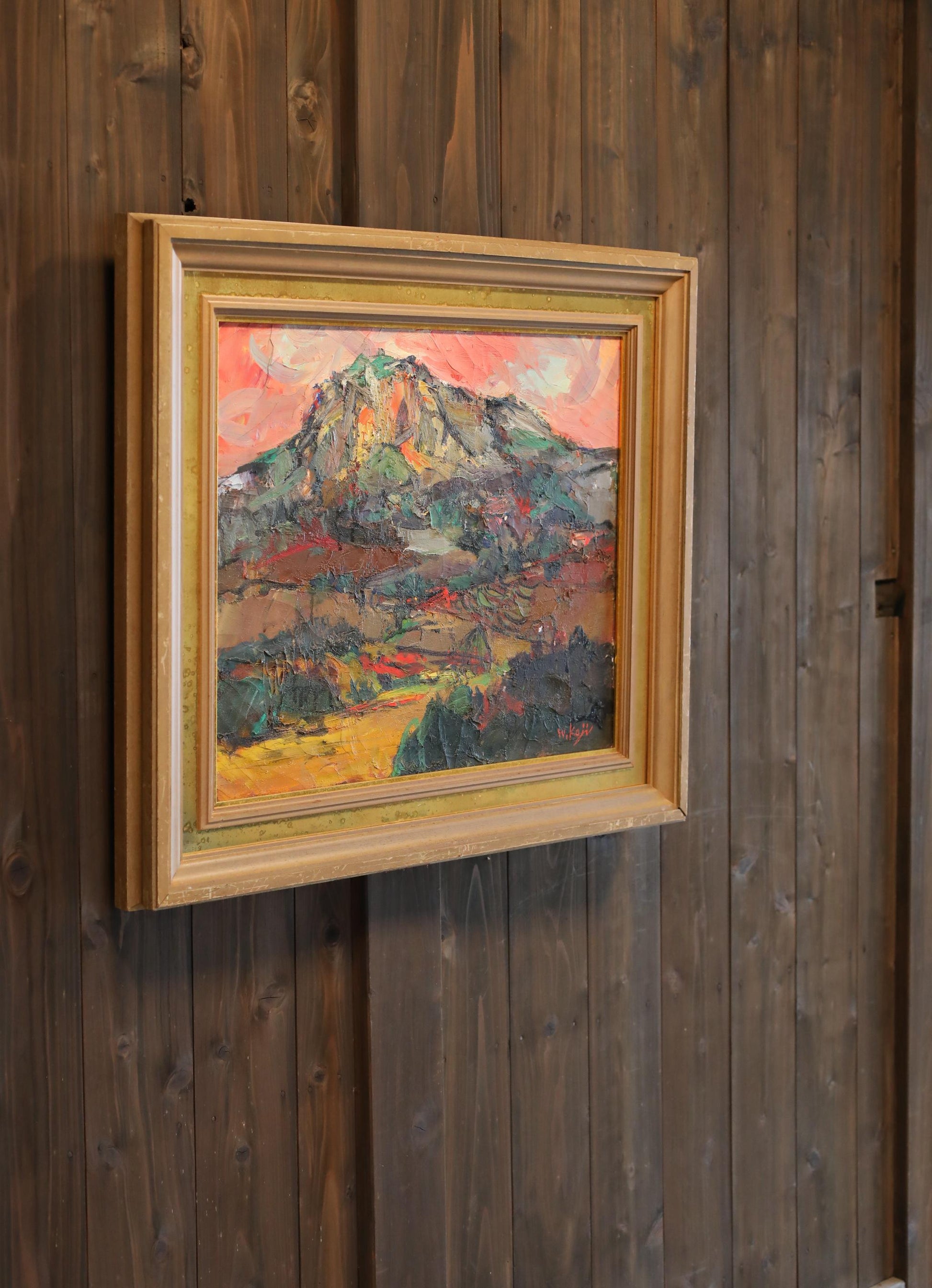 a framed painting of a mountain landscape hanging on a wooden wall.