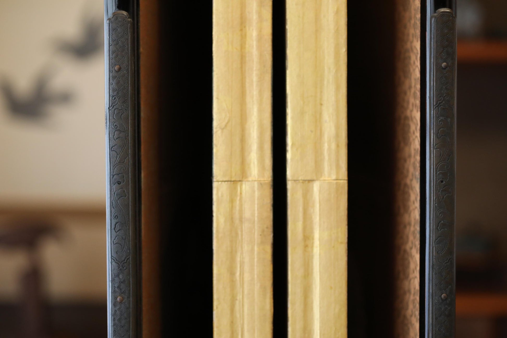 a close-up view of a wooden door frame with two vertical wooden panels, one on each side, with a black metal frame. The background is blurred, making the door frame the main focus of the image.