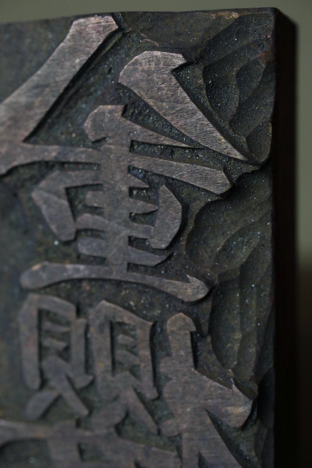 a close-up view of a dark, textured surface with a carved or engraved design. The design appears to be a symbol or text, but it is not possible to determine the exact meaning or significance of the symbol or text from the image alone.