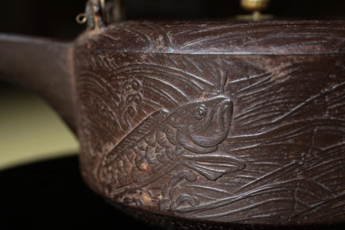 A close-up image of a dark brown, intricately carved metal object with a fish-like design on its surface.