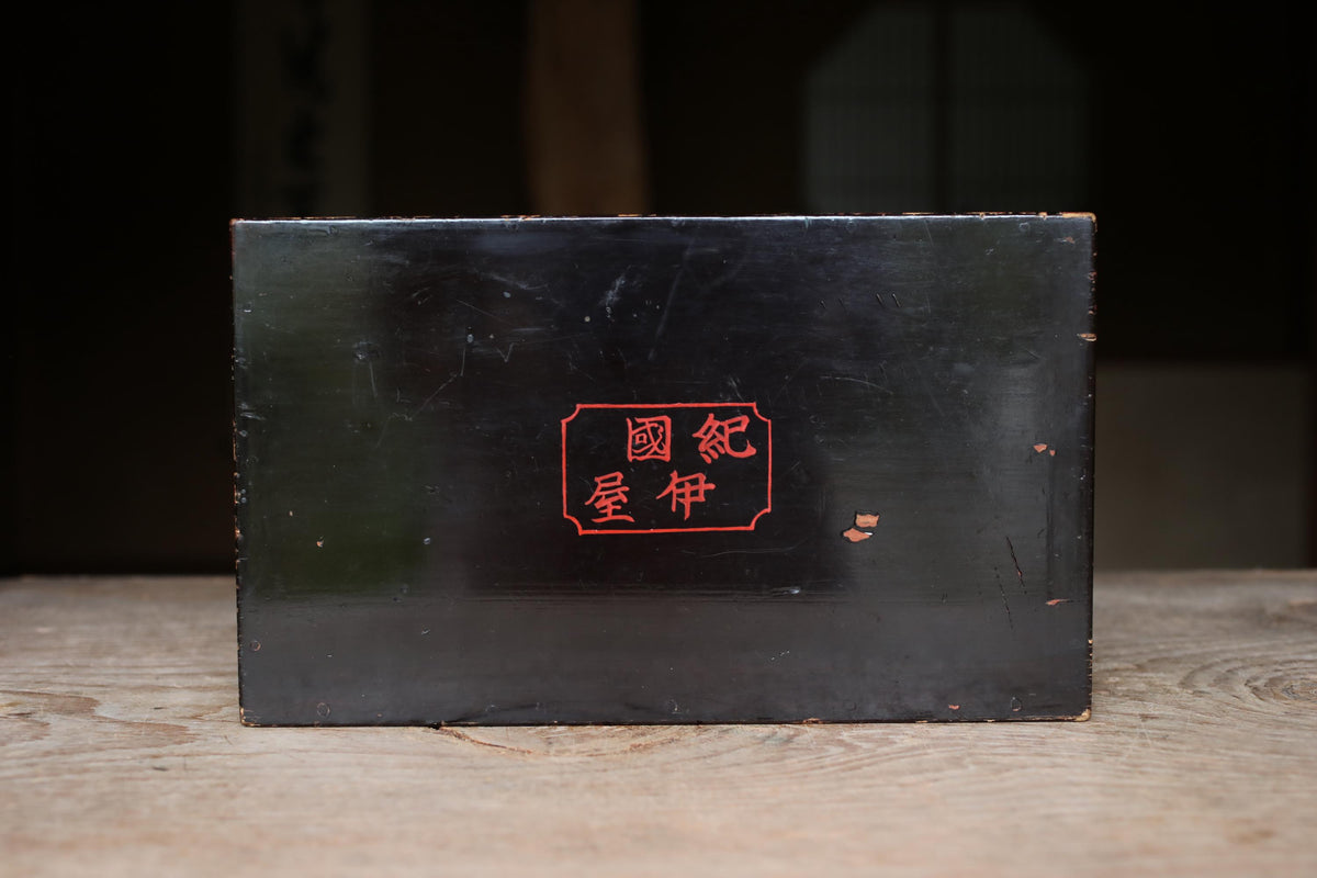 A black rectangular box with red Chinese characters on it, placed on a wooden surface.