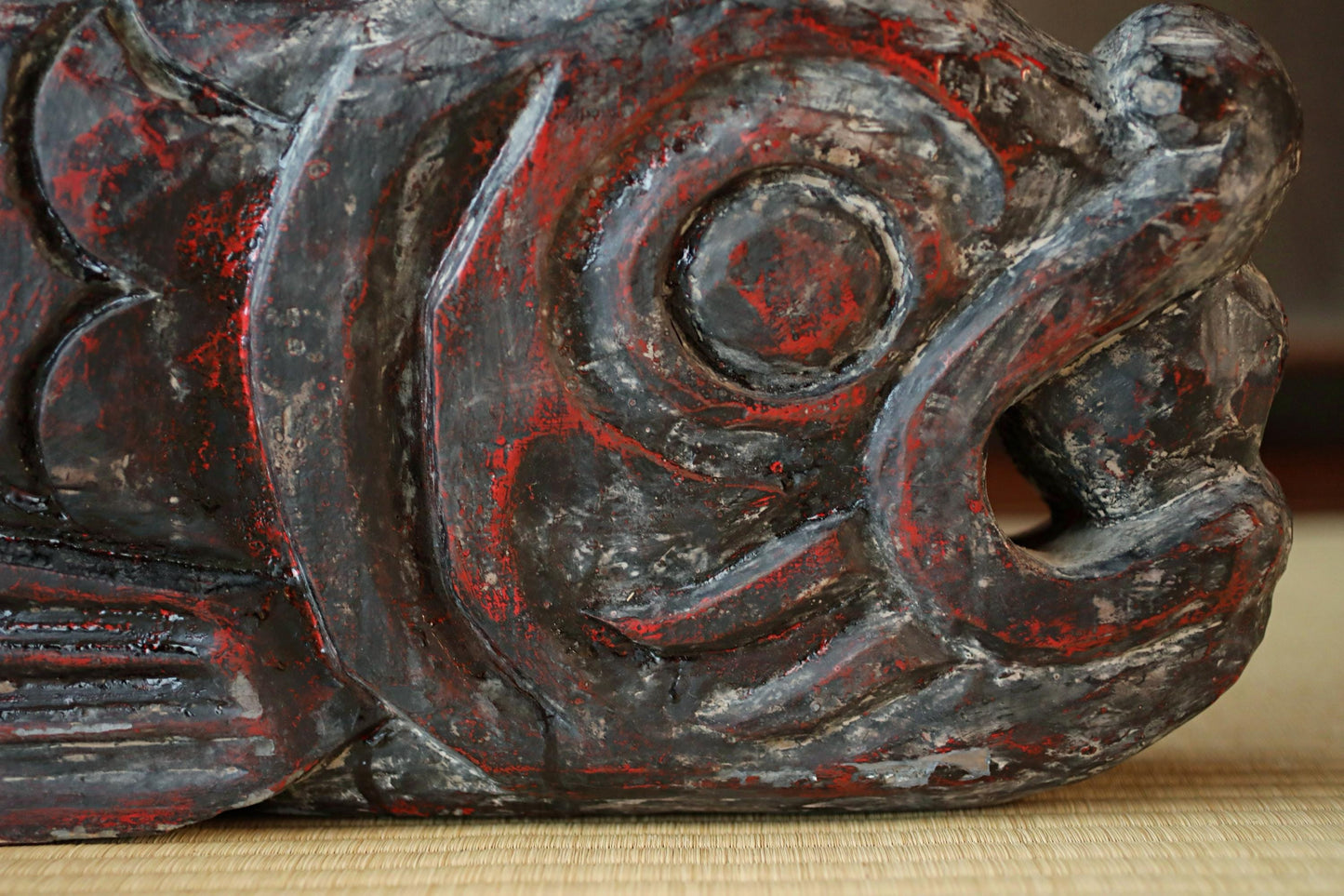 a close-up view of a weathered, dark-colored wooden sculpture with a red and black pattern.