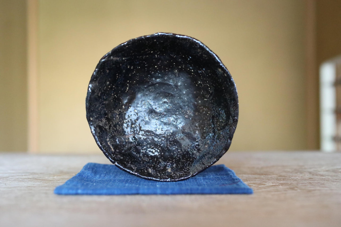 A black, textured bowl sits on a blue cloth on a wooden surface.
