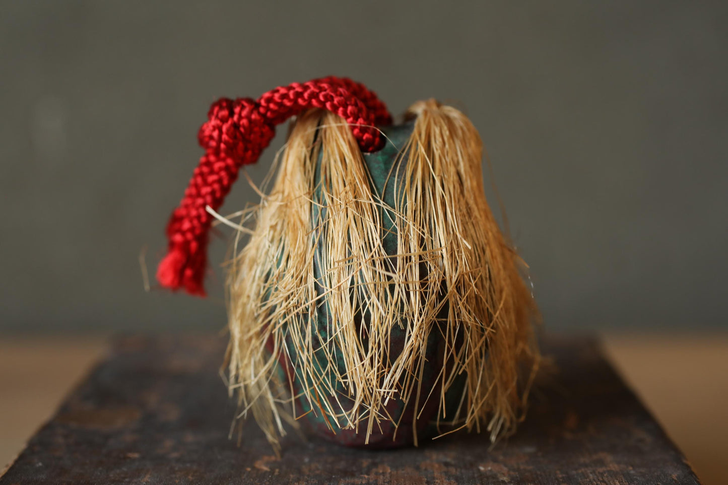 A small, round vase with a red string tied around it, placed on a dark surface.