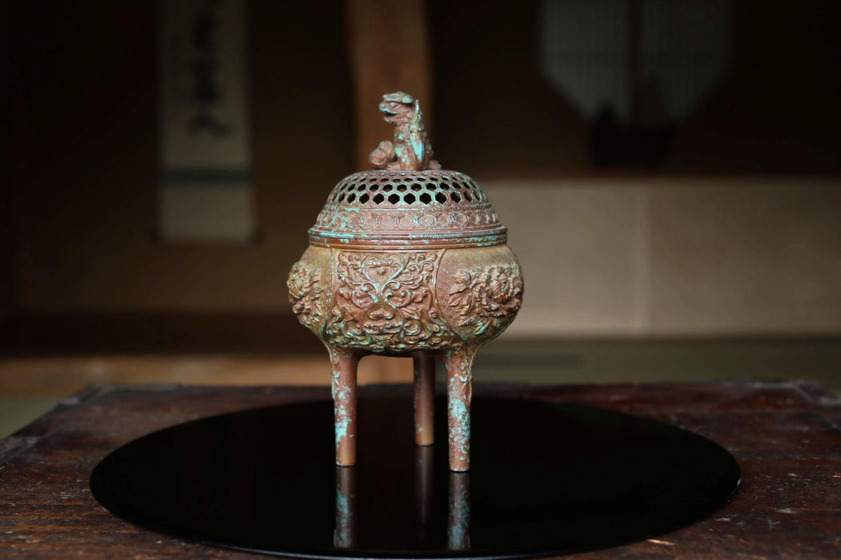 An ornate bronze incense burner with a dragon design sits on a black circular tray.