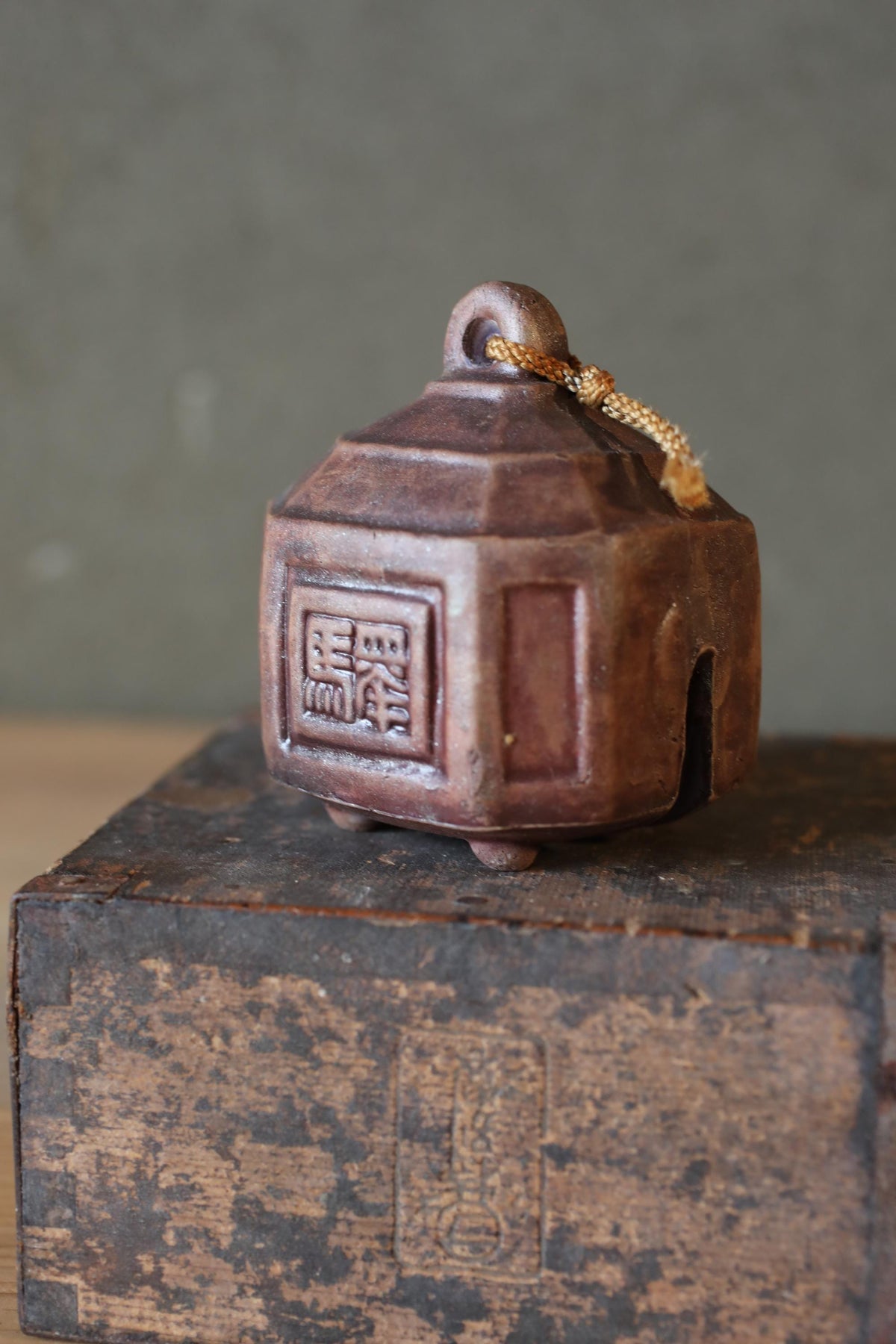 An old, weathered ceramic bell with a wooden base sits on a wooden surface.