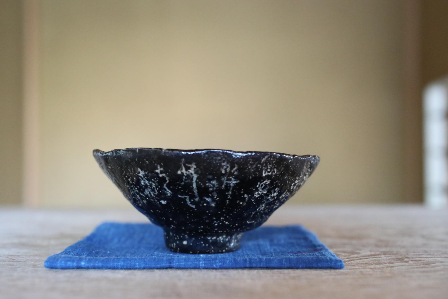 A black ceramic bowl with white speckles sits on a blue cloth on a wooden surface.