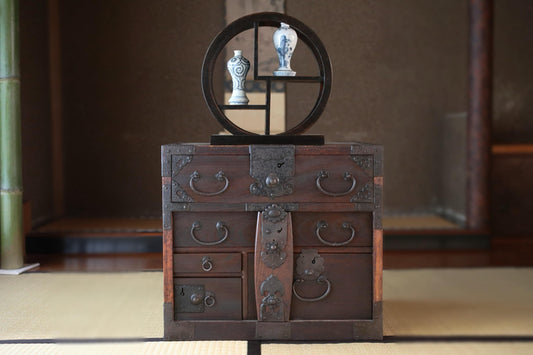 a traditional Japanese wooden chest with intricate metalwork and handles, placed on a tatami mat.