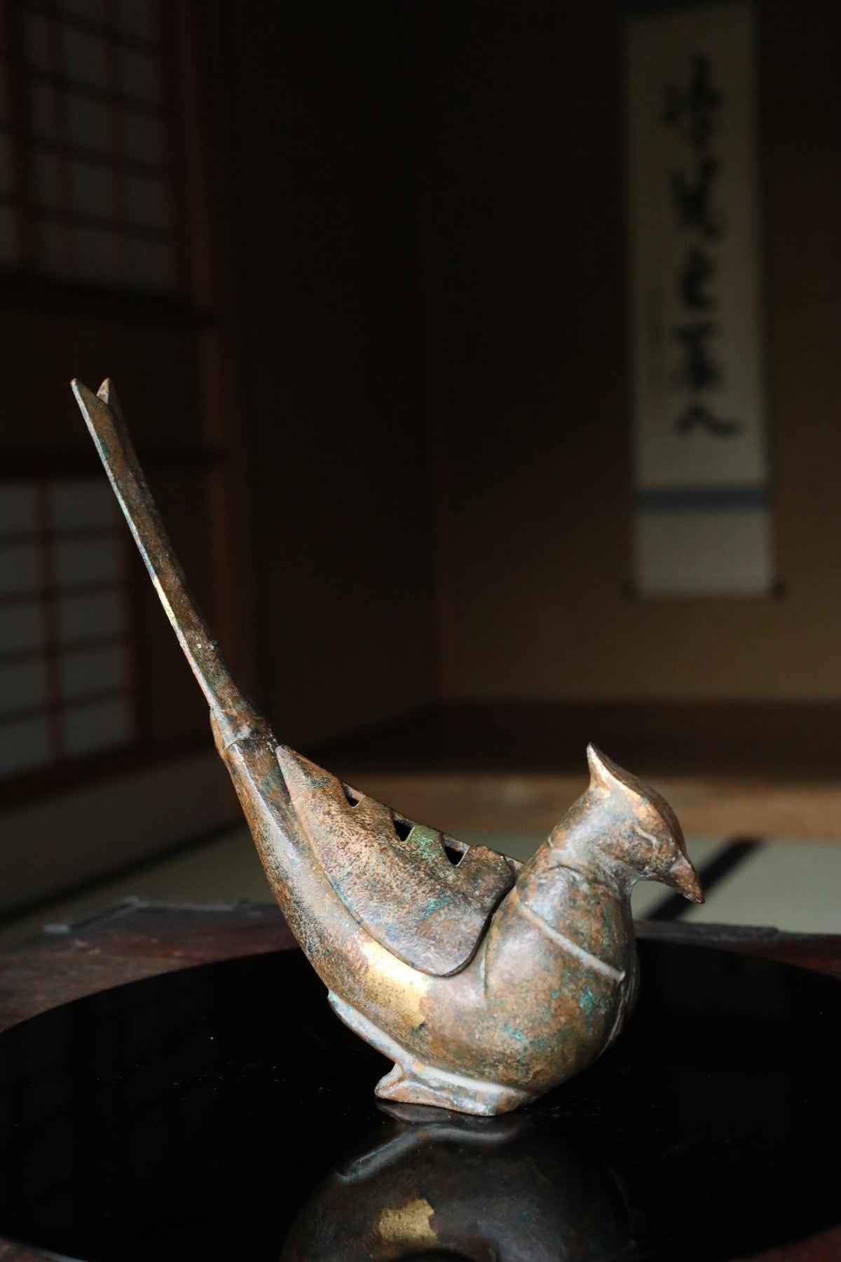 A bronze bird figurine with a long, curved beak and a small tail is sitting on a black surface.