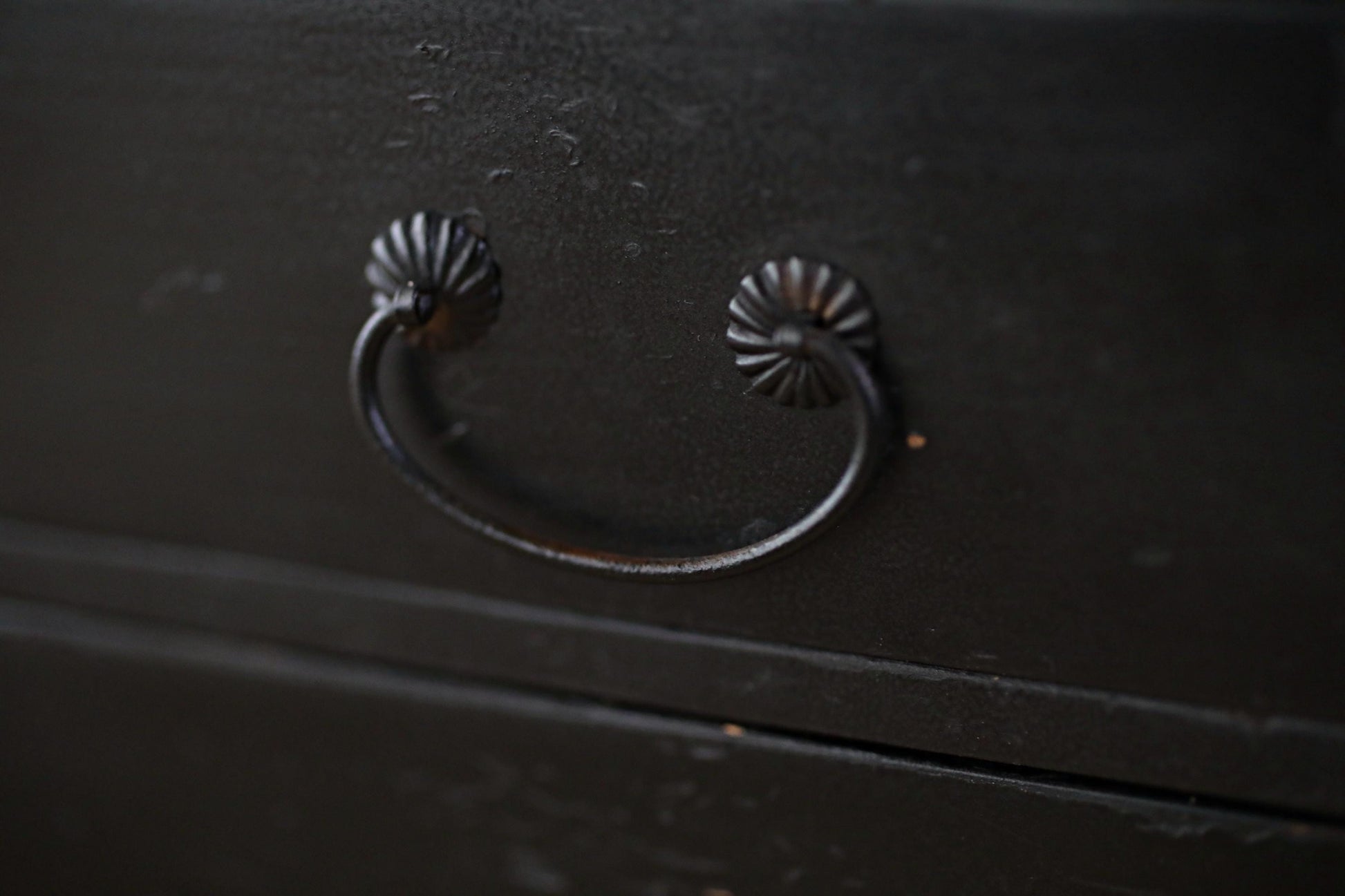 A close-up view of a black metal drawer handle with a curved design.