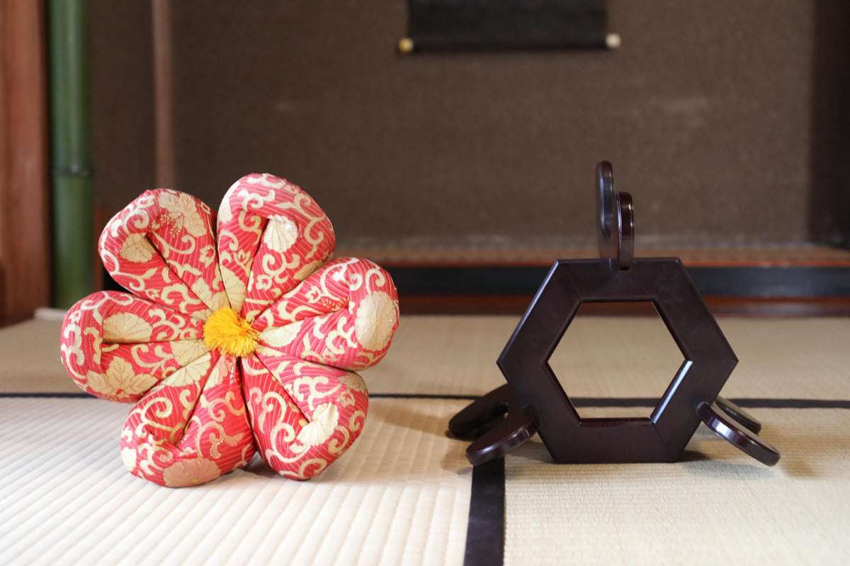 a red and white flower-shaped object with a yellow center, placed on a white surface next to a black hexagonal object.