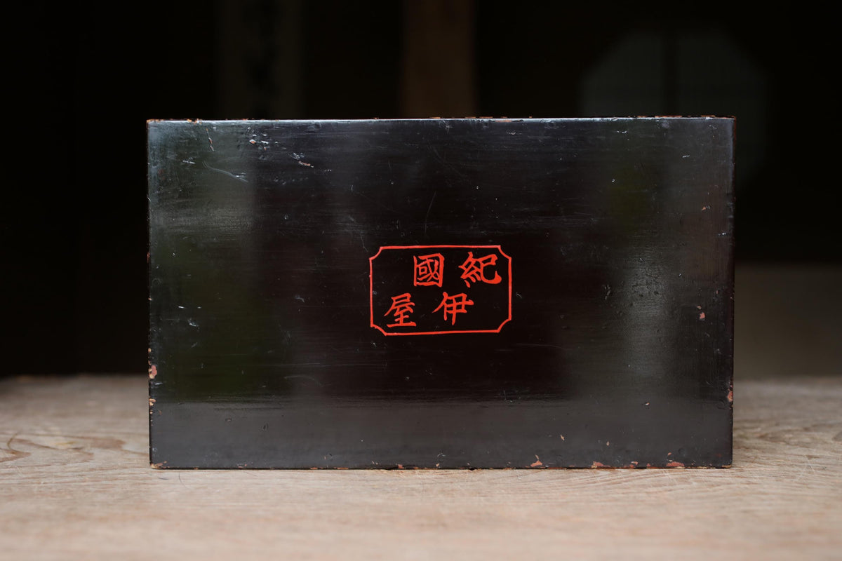 A black rectangular box with a red Chinese character on it, placed on a wooden surface.