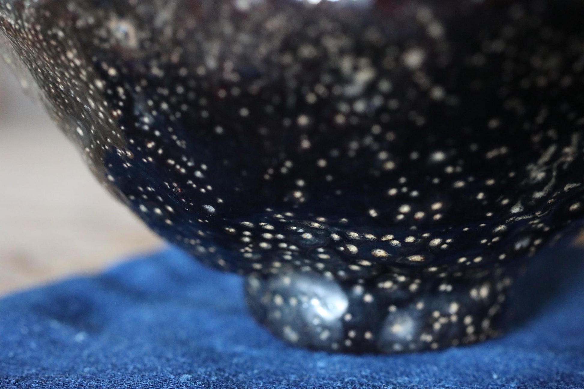 A close-up view of a black, speckled ceramic bowl or vase, with a blue cloth or surface underneath it.