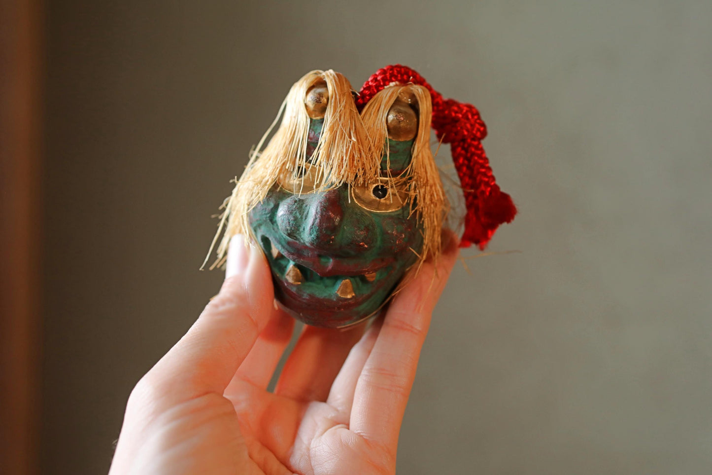 A hand holding a small, colorful figurine with a red ribbon around its neck.