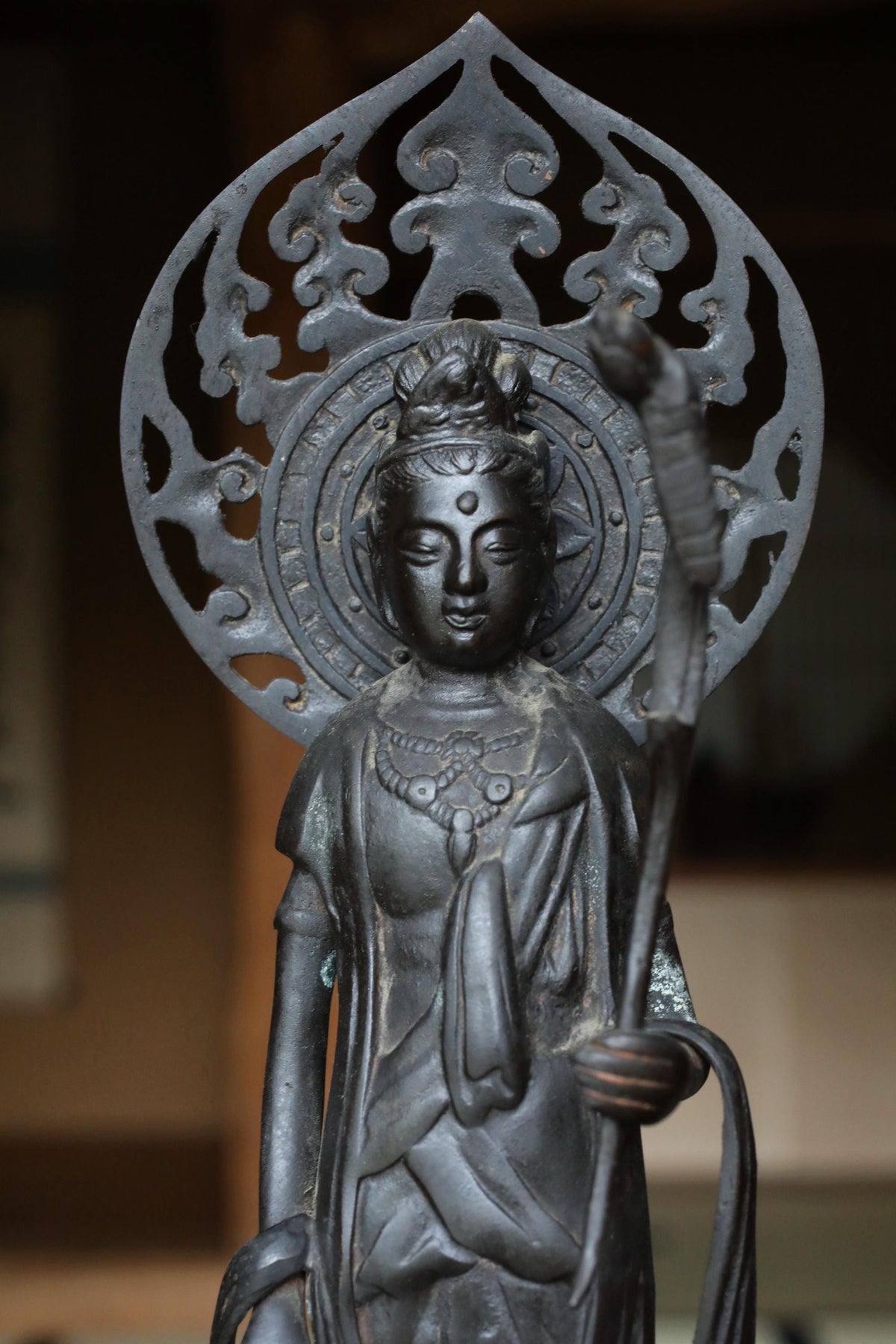 A bronze statue of a deity with an ornate headdress and holding a staff, standing in a temple setting.