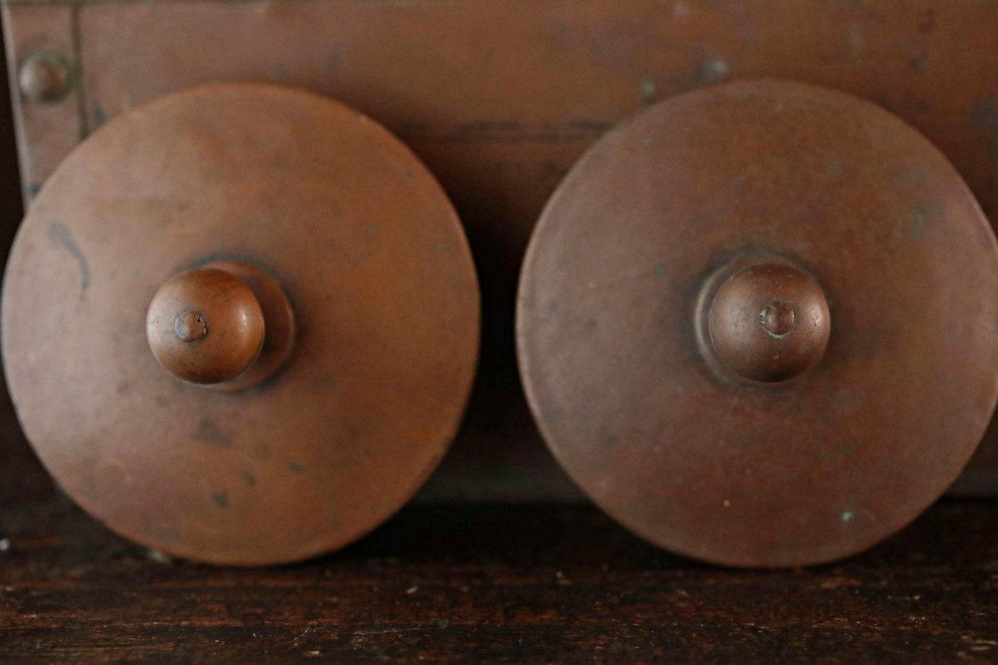 Two round, brown metal objects with a metallic finish are placed side by side on a wooden surface.
