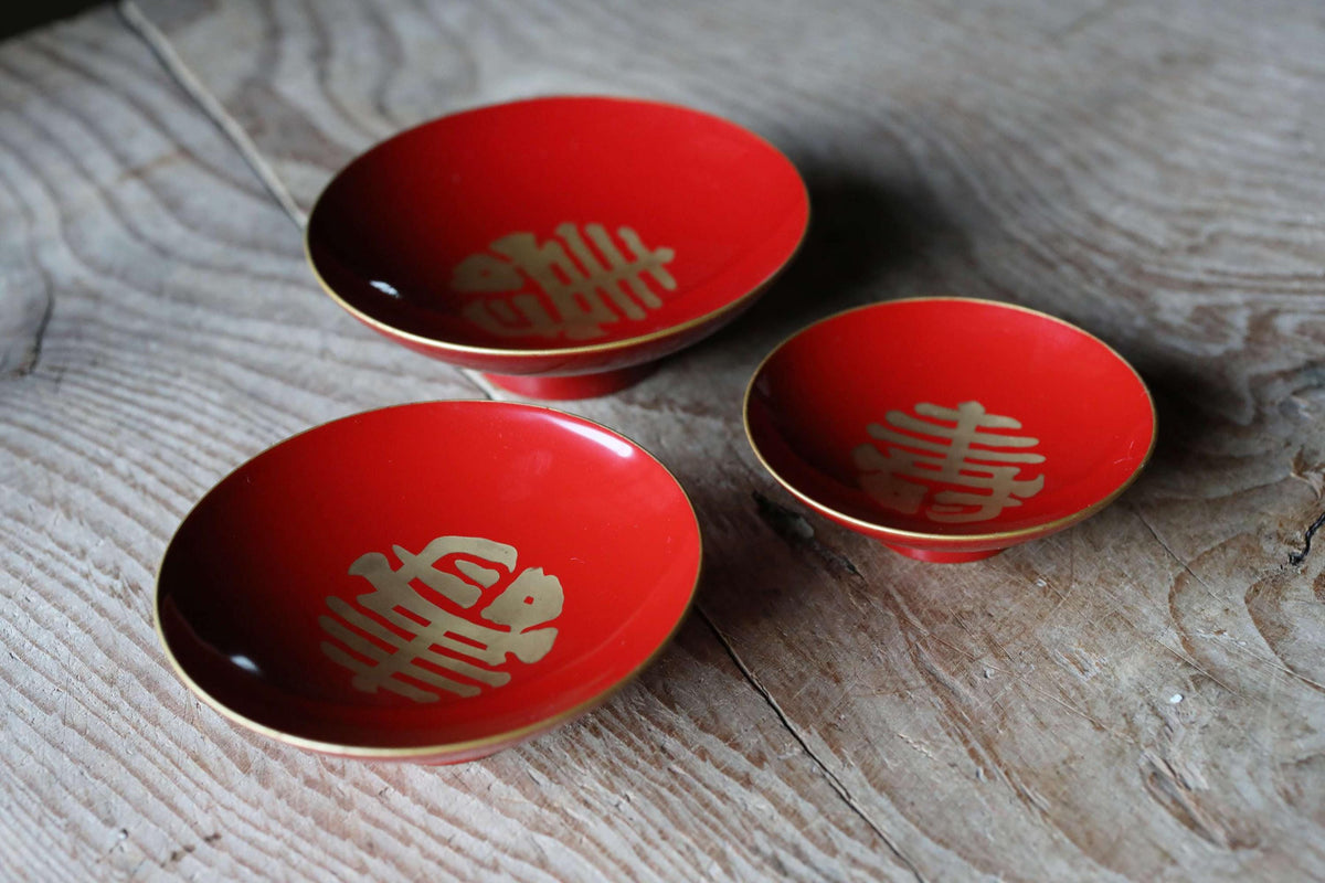 Three red bowls with gold designs are placed on a wooden surface.