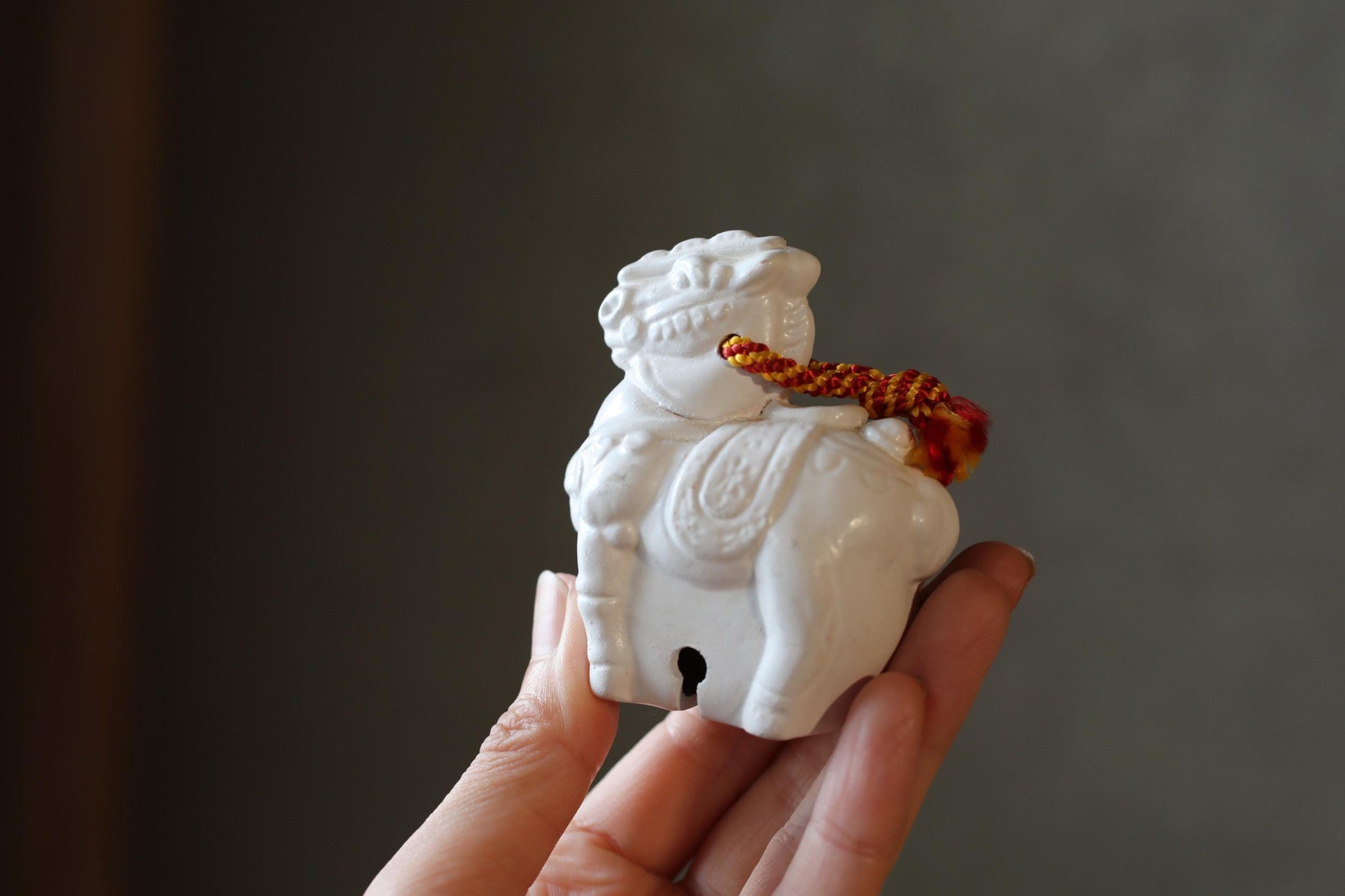 A person's hand holding a small white ceramic figurine with a red and yellow string around its neck.