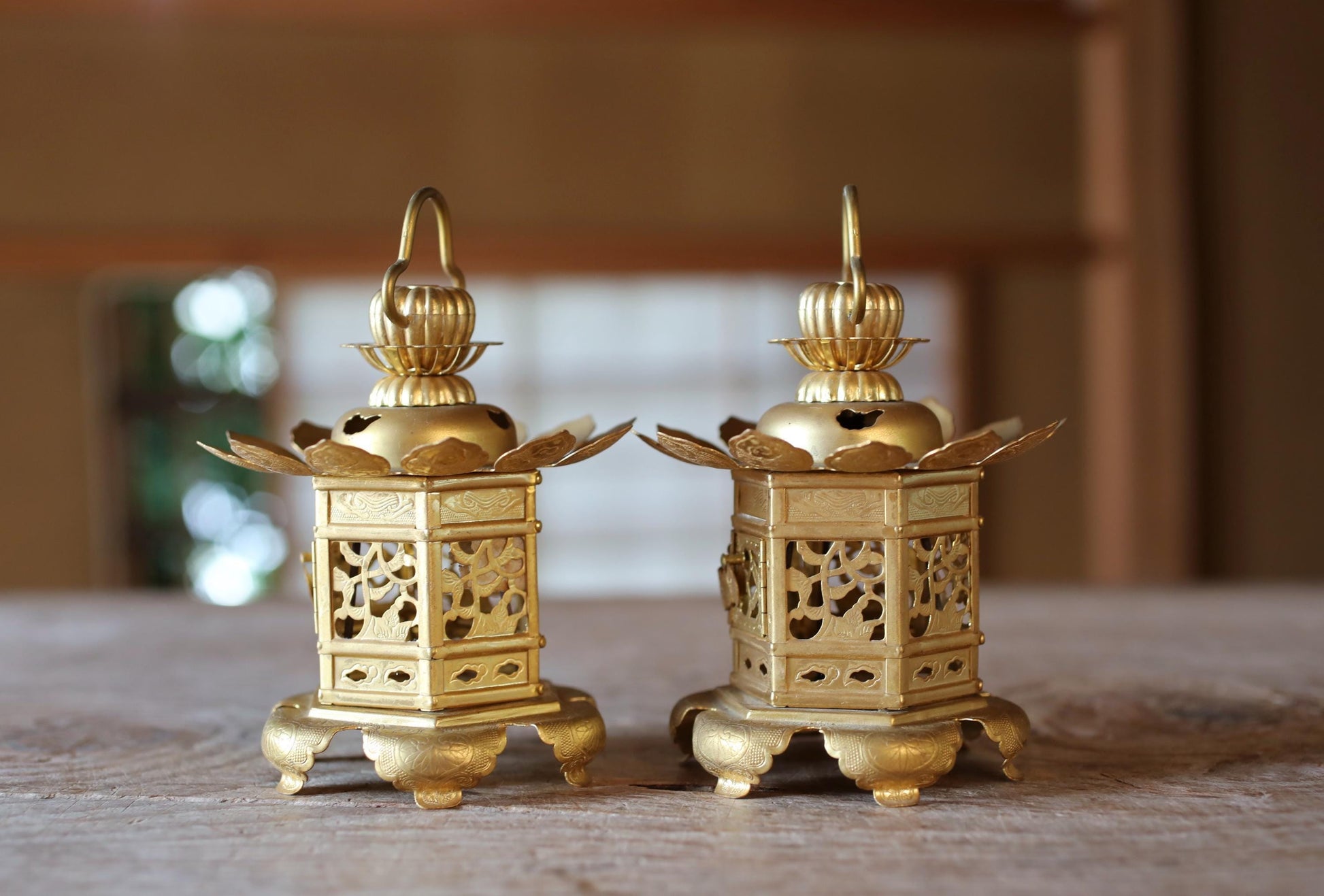Two ornate golden lanterns with intricate designs are displayed on a wooden surface.