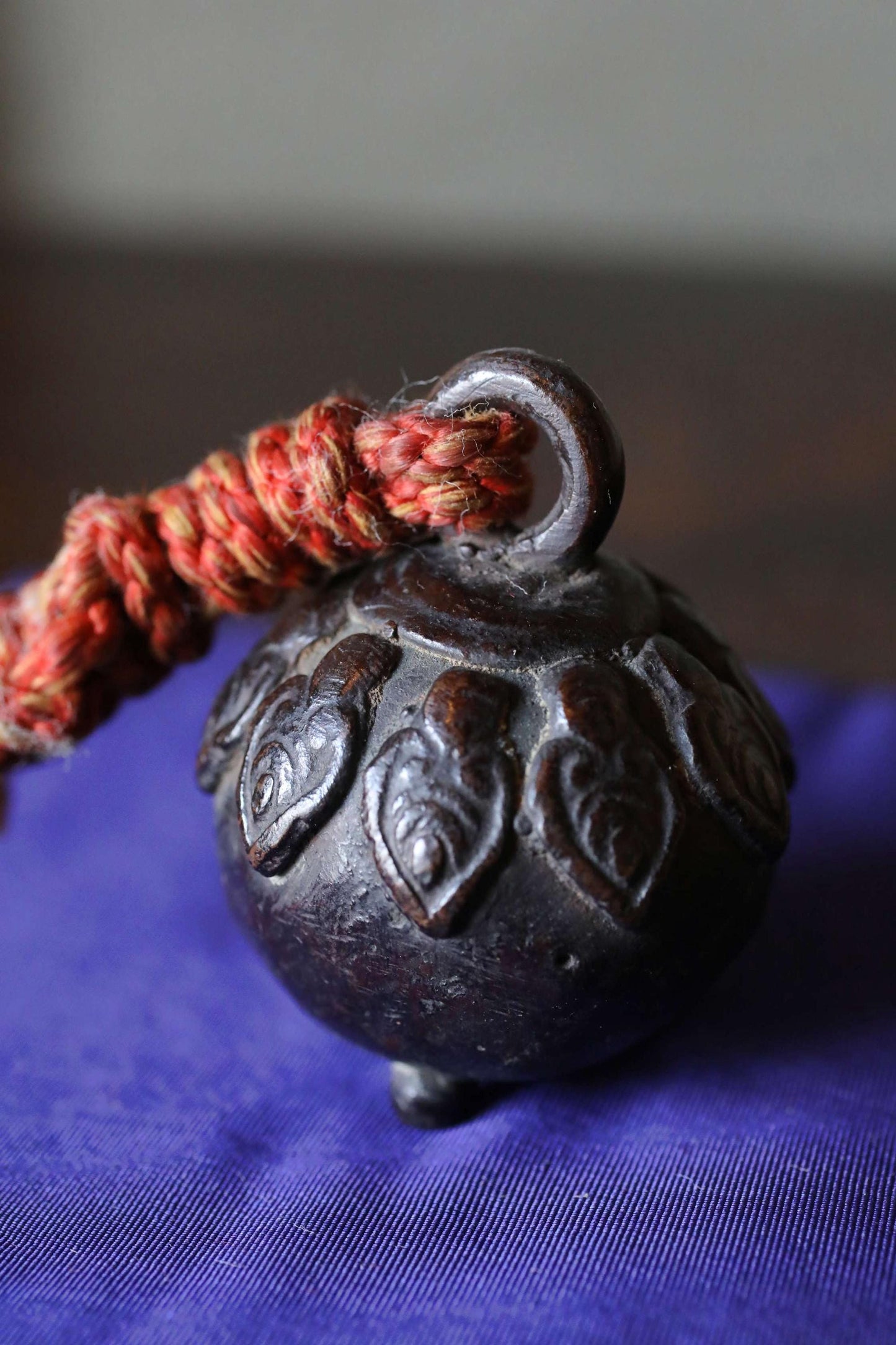A dark metal bell with a red string attached to it, resting on a blue fabric surface.