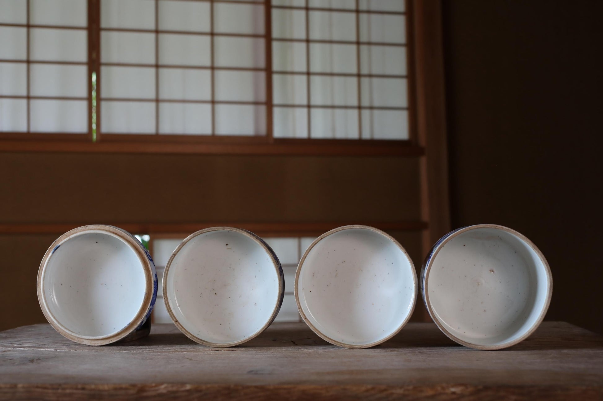 Four white ceramic bowls arranged in a row on a wooden surface, with a window and wooden frame in the background.