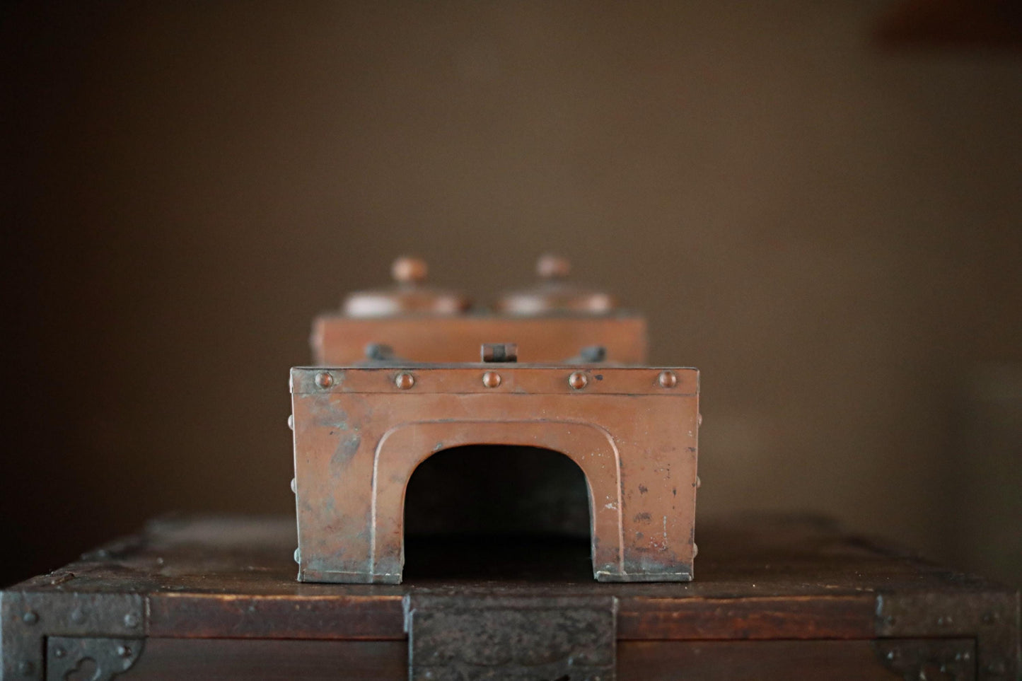 a small, antique-looking metal box with a curved arch on top, sitting on a wooden surface.