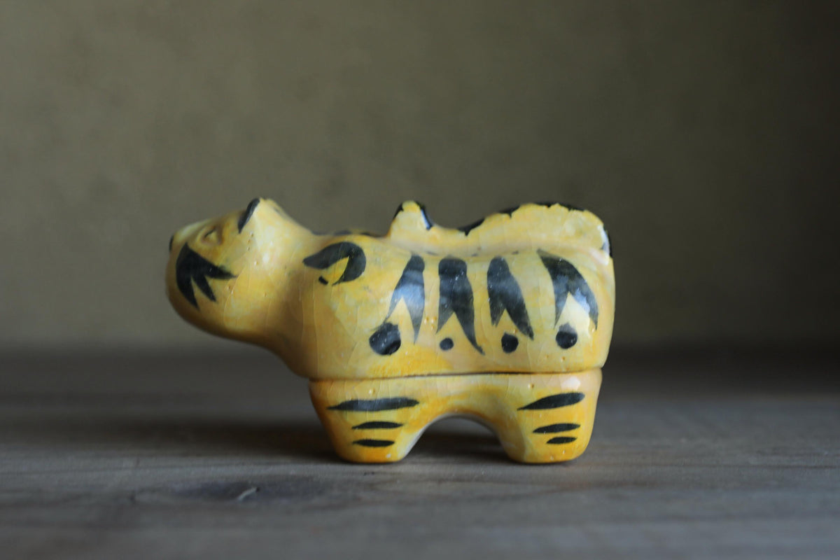A yellow and black ceramic hippo figurine is sitting on a wooden surface.