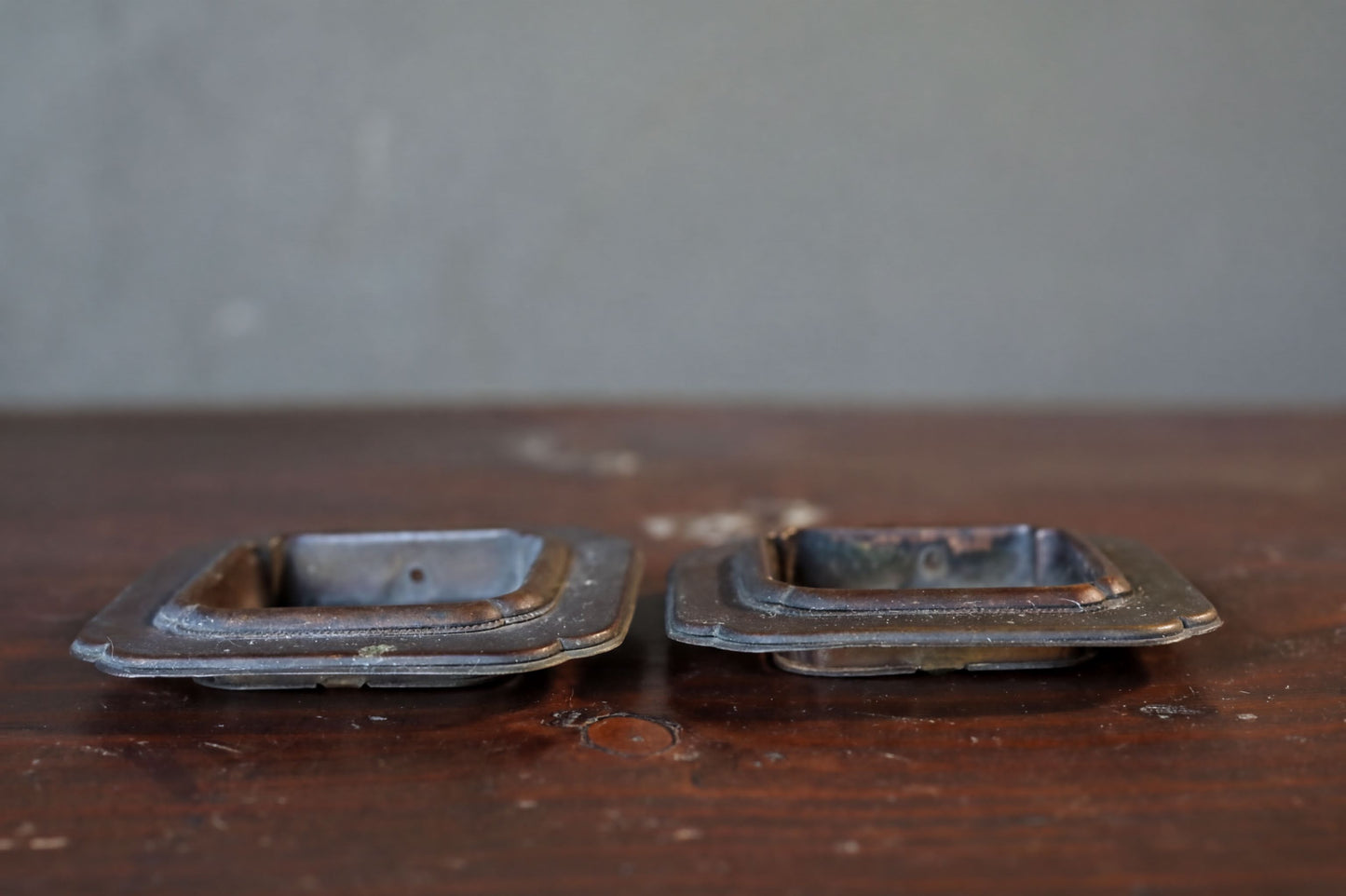 Two old, square metal handles are placed on a wooden surface.